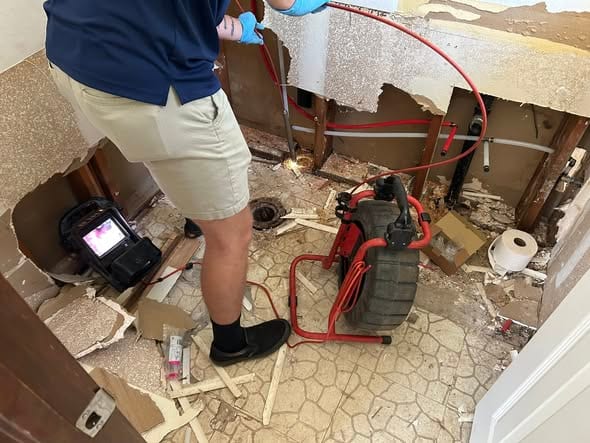 Plumber running a sewer camera in a demoed bathroom, with the camera reel and monitor set up on the floor