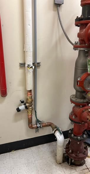 New copper connection with relief valve and gauge beside a fire riser in a commercial mechanical room