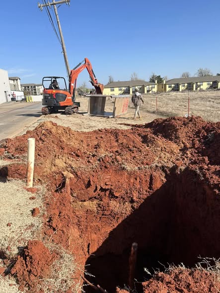 Ultimate Plumbing technician operating a mini-excavator to carefully expose a broken residential sewer line without damaging the surrounding fence.