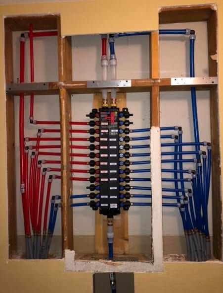 New PEX manifold installed in the wall with red hot and blue cold lines routed neatly through the framing