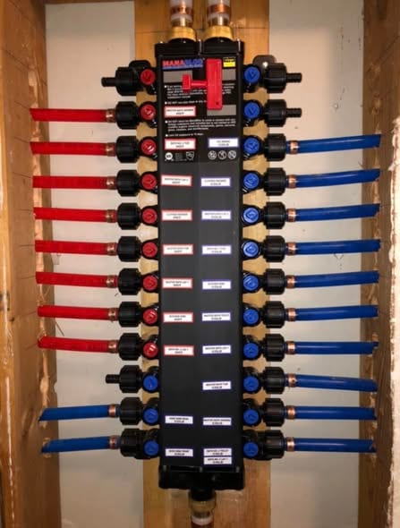 Close-up of a labeled MANABLOC PEX distribution manifold with red hot-side and blue cold-side ports