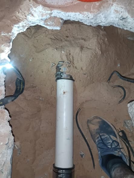 New PVC drain pipe standing in a hand-dug excavation beneath a slab during a sewer line repair