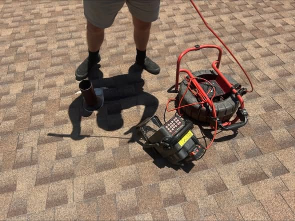 Sewer camera reel and monitor staged on a roof beside the vent stack for a drain line inspection