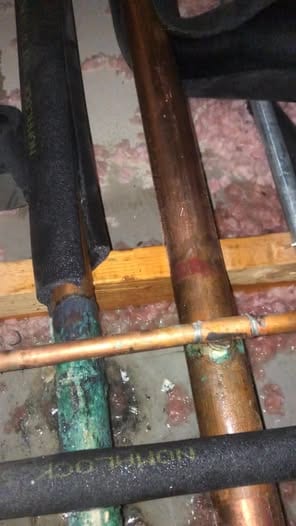 Copper water lines in an attic with heavy green corrosion at a joint, insulation pulled back for the repair