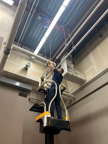 Plumber on a lift making an overhead pipe repair at the ceiling of a commercial building