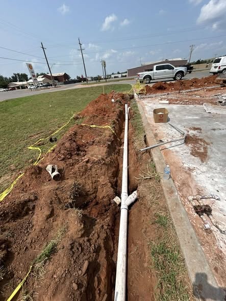 New sewer line laid in an open trench beside a commercial parking lot