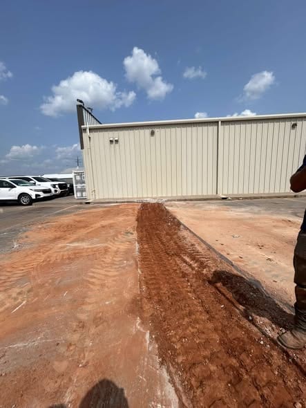 Backfilled trench line running across the lot to a commercial building after sewer replacement
