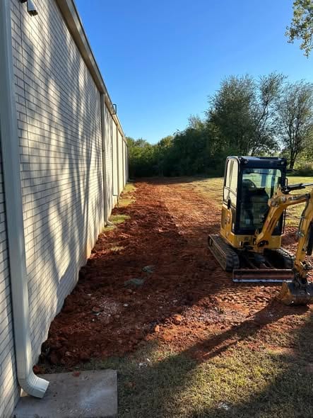 Backfilled sewer trench along the side of a commercial building with the mini excavator parked at the end