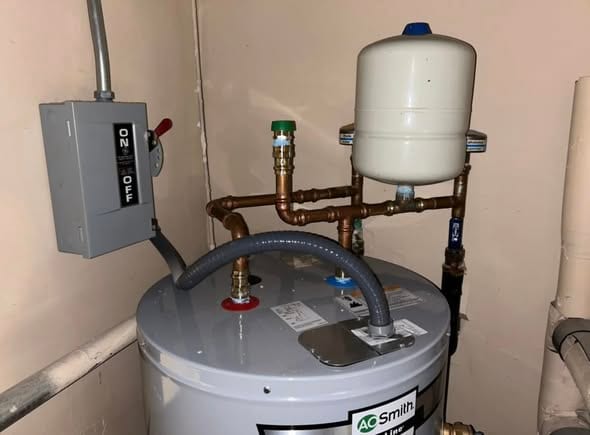 Top of a new water heater showing the copper manifold, expansion tank, and flex line connections