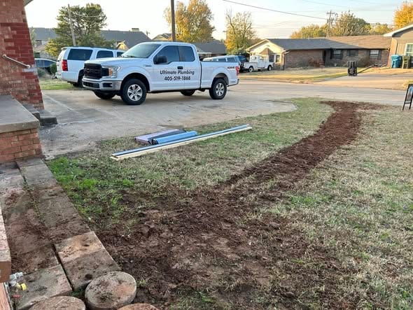 Fresh backfilled water line path across a front yard with the Ultimate Plumbing truck at the curb
