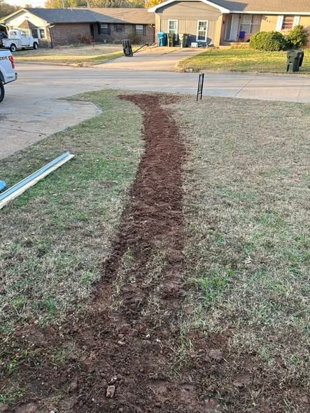 Backfilled trench path of a rerouted water service line running across the yard to the house