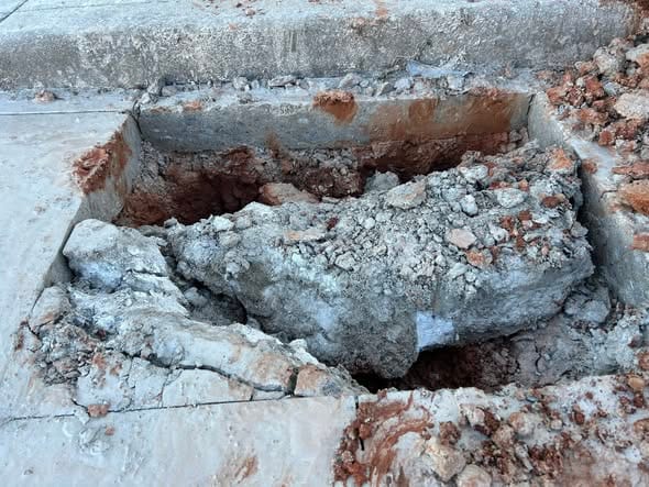 Rectangular cut through the slab with broken concrete lifted out over the pipe trench