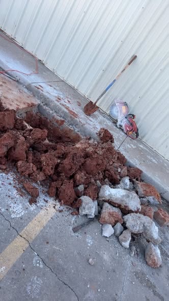 Sawcut concrete opened along the building with red clay spoil piled and the cut saw on site