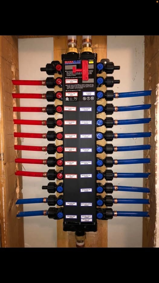 Labeled MANABLOC PEX distribution manifold with red hot and blue cold ports in open framing